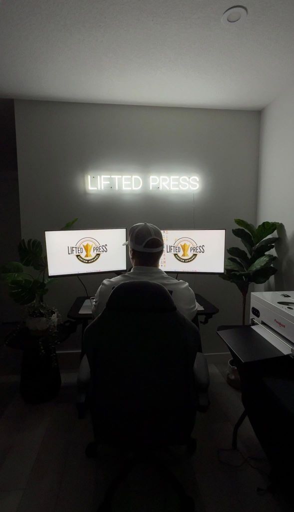 Lifted Press owner at the design desk, preparing artwork under the Lifted Press neon sign